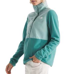 A two-toned teal North Face Glacier Fleece Pullover with a high collar, partial button-up front, and a logo on the chest, paired with white pants.