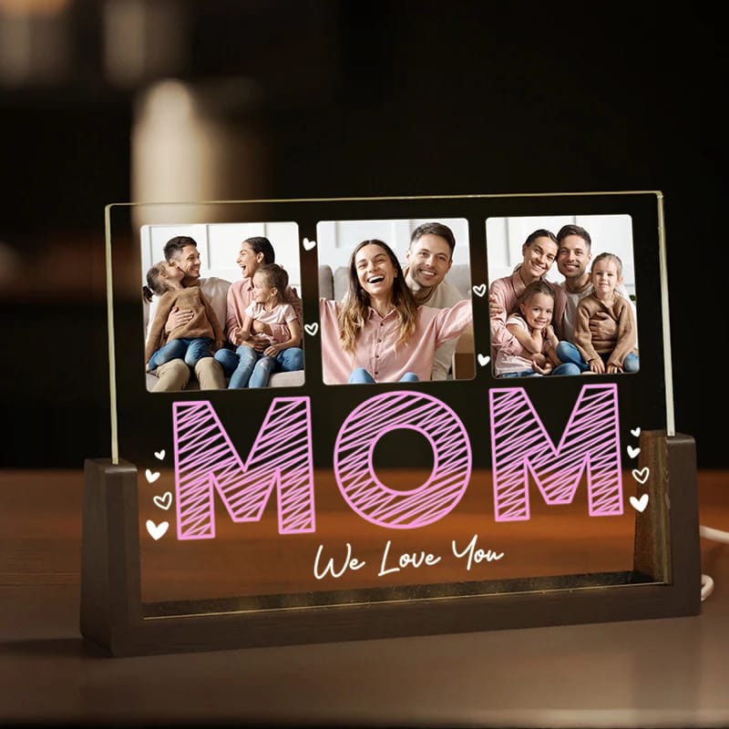 A personalized night light with \“MOM\“ illuminated in pink, featuring three family photos above, framed in a dark wooden base with heart accents and the phrase \“We Love You\“ in elegant script below.