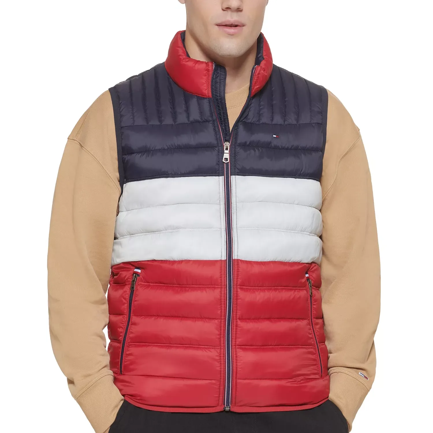 A color-blocked puffer vest featuring navy, white, and red horizontal stripes with a front zipper, worn over a beige sweatshirt.