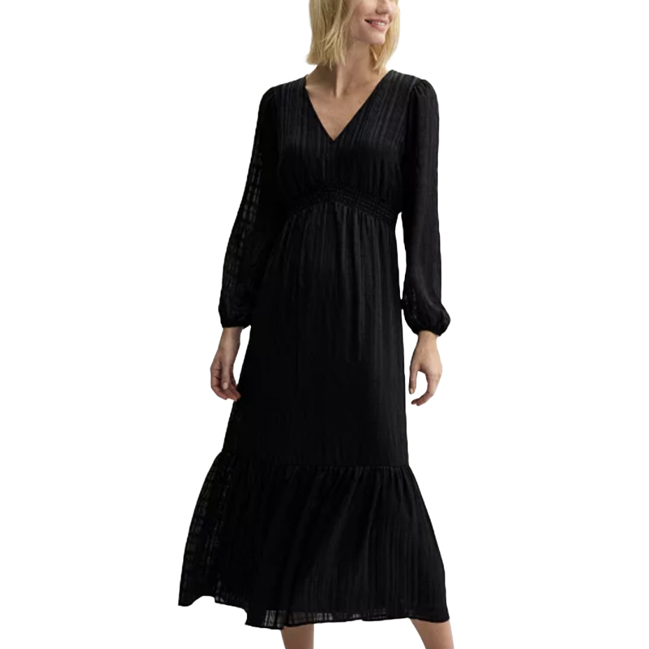 A woman is wearing a long, black, V-neck dress with long sleeves and an empire waist. The dress has a subtle texture and a tiered hem.
