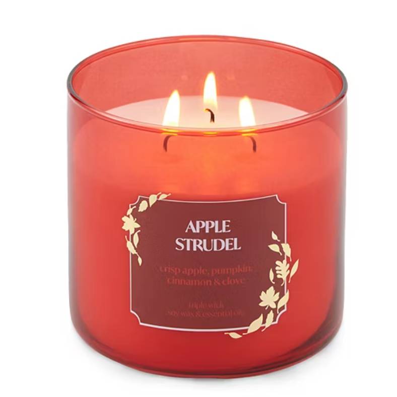 Red jar candle labeled \“Apple Strudel,\“ featuring scents of crisp apple, pumpkin, cinnamon, and clove, with three wicks and made from soy wax and essential oils.