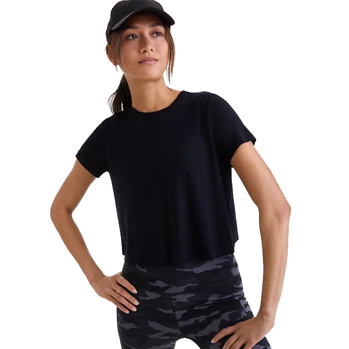 A woman wearing a black short-sleeve top and camo leggings, accessorized with a black cap.