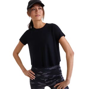A woman wearing a black short-sleeve top and camo leggings, accessorized with a black cap.