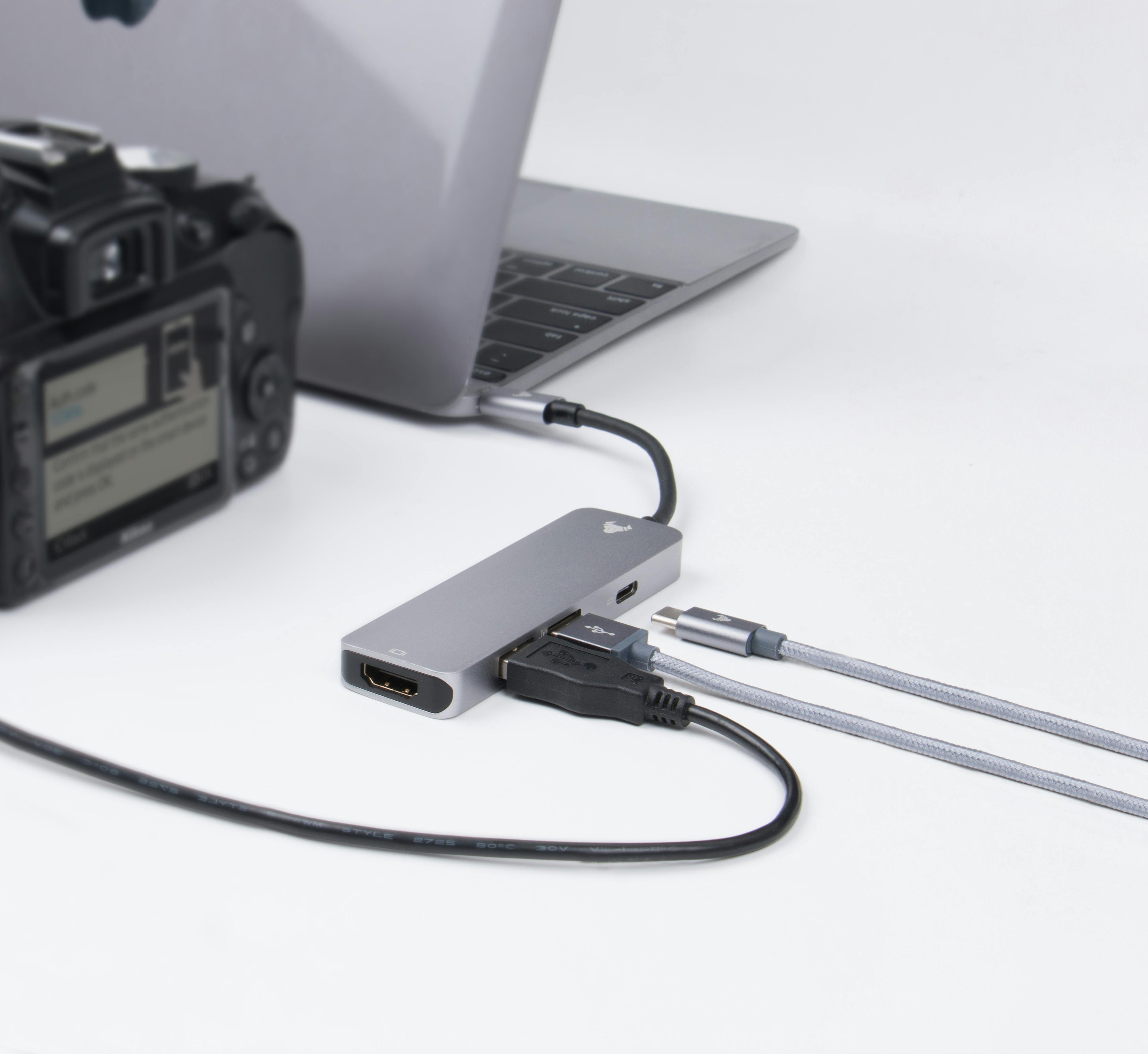 Laptop, USB-C hub adapter, cable, and digital camera on a white background.
