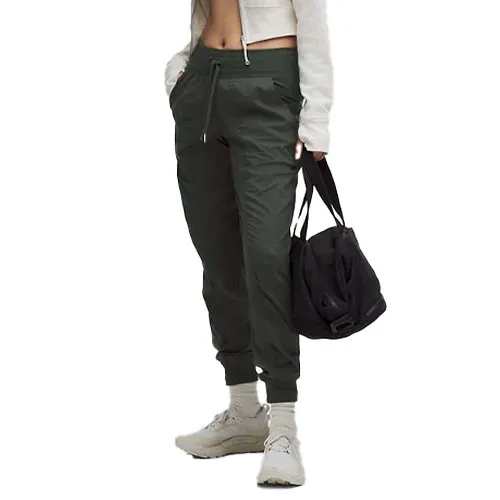 A person wearing dark green jogger pants, beige socks, and beige sneakers, holding a black sports bag.