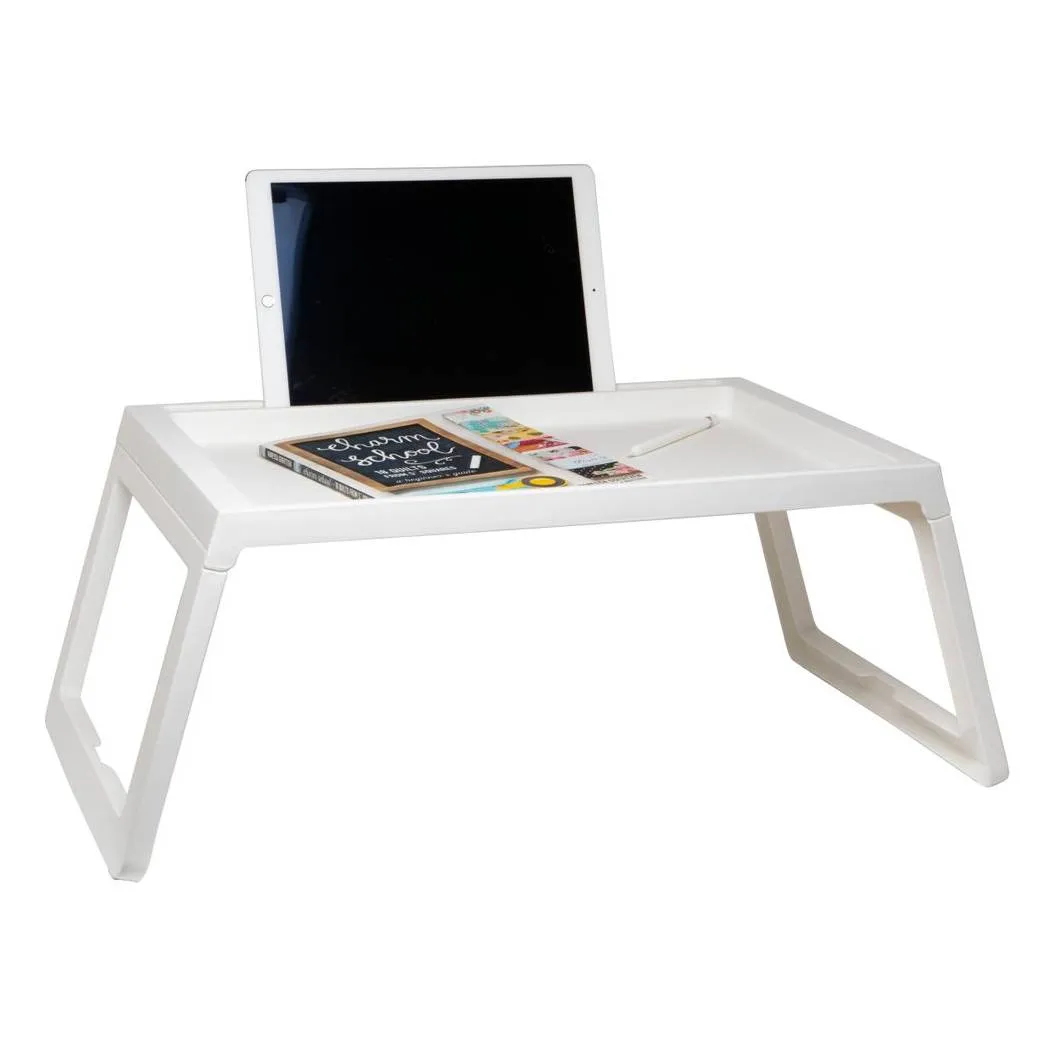 A white portable lap desk with foldable legs, featuring a slot for a tablet and space for items like a notebook and pen on its surface.