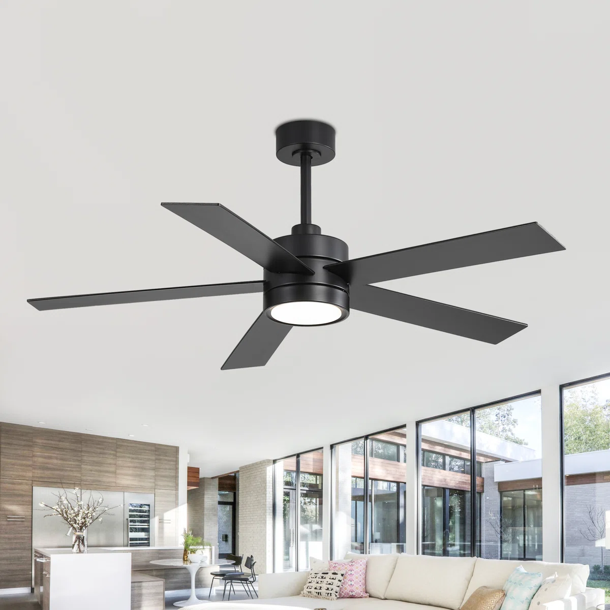 A modern black ceiling fan with five blades and integrated light fixture is installed in a spacious, contemporary living room with large windows, a white sofa, and a minimalist décor.