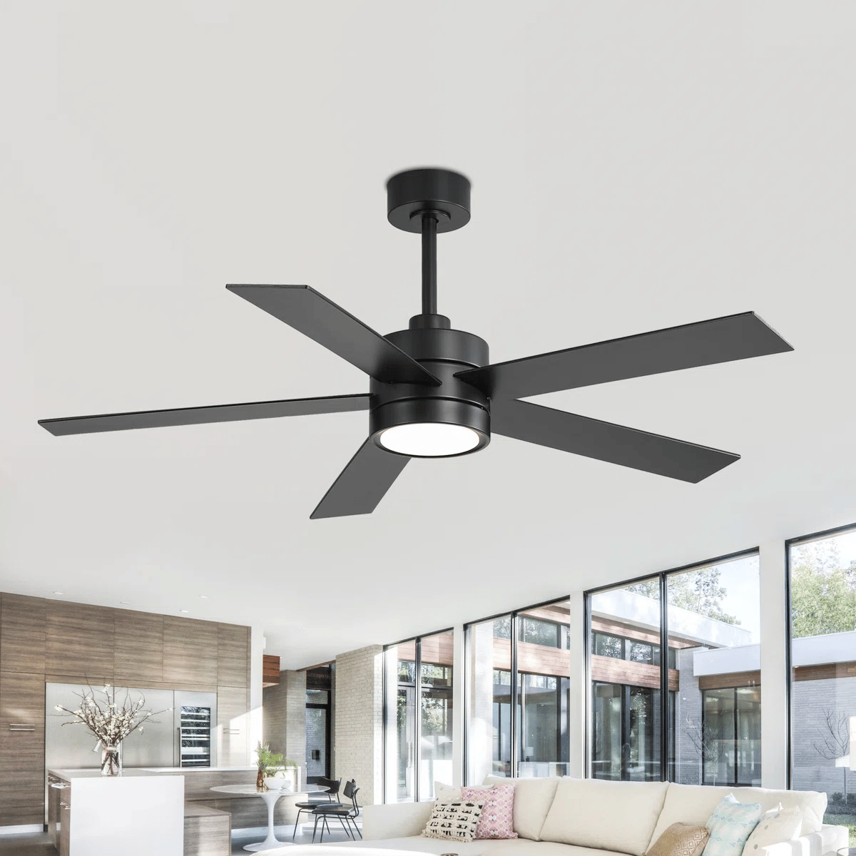 A modern black ceiling fan with five blades and integrated light fixture is installed in a spacious, contemporary living room with large windows, a white sofa, and a minimalist décor.