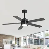 A modern black ceiling fan with five blades and integrated light fixture is installed in a spacious, contemporary living room with large windows, a white sofa, and a minimalist décor.