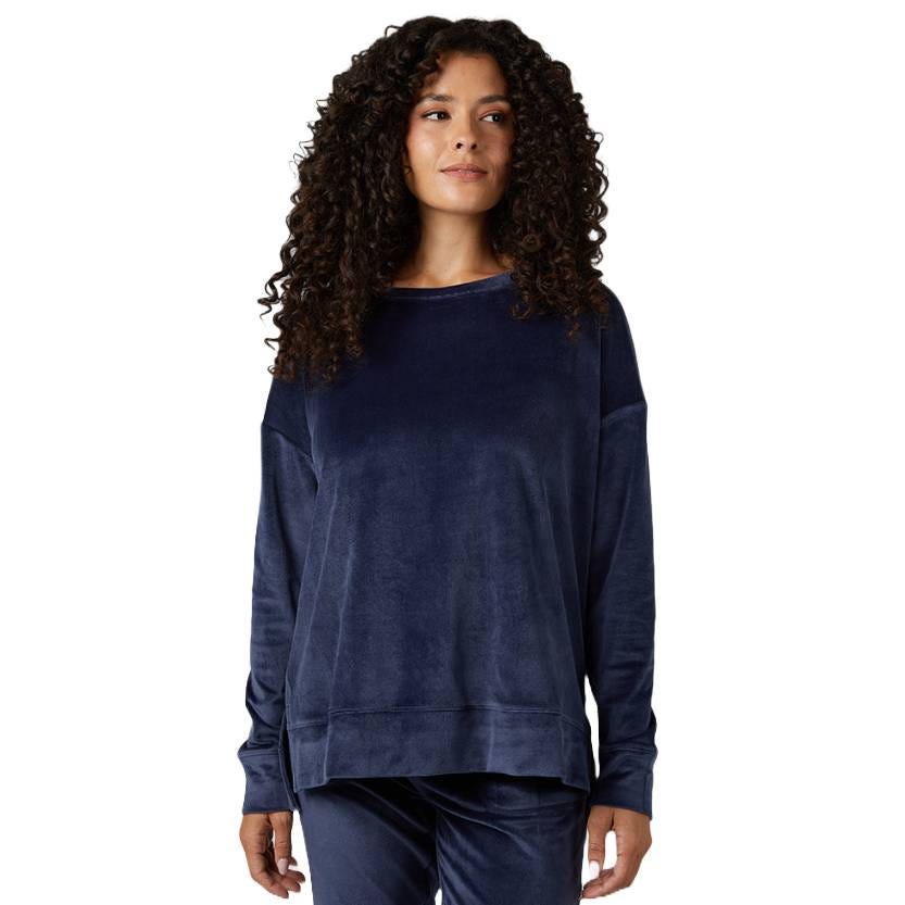 A woman is wearing a navy blue velour lounge set with a long-sleeve top and matching pants.
