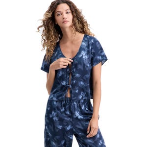 A woman is wearing a short-sleeved, deep V-neck top and pants set with a blue floral pattern, featuring ties at the front and an elastic waistband.