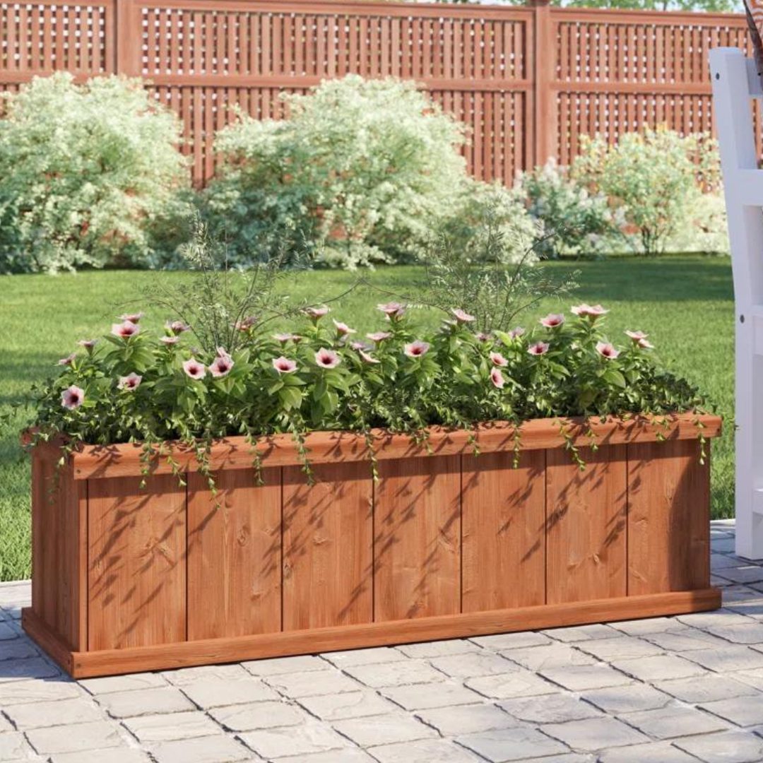 A wooden rectangular planter box filled with flowering plants on a paved outdoor surface.