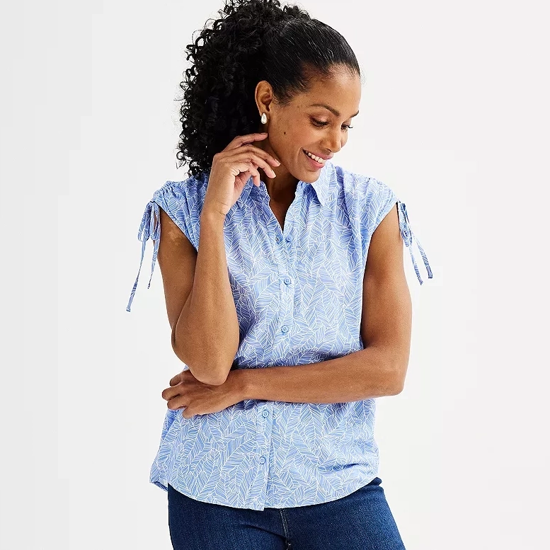 A woman wearing a blue patterned short-sleeve blouse with tie details on the sleeves and denim pants.
