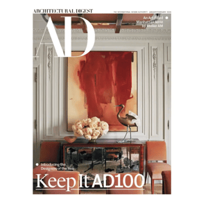 Architectural Digest cover showing an art-filled room by Atelier AM with a striking red abstract painting, floral arrangement, and decorative sculpture on a mirrored console, accompanied by stylish seating.