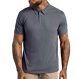 A person wearing a short-sleeve, blue-grey polo shirt with a button-up collar and beige pants. Tattoos are visible on the arms.