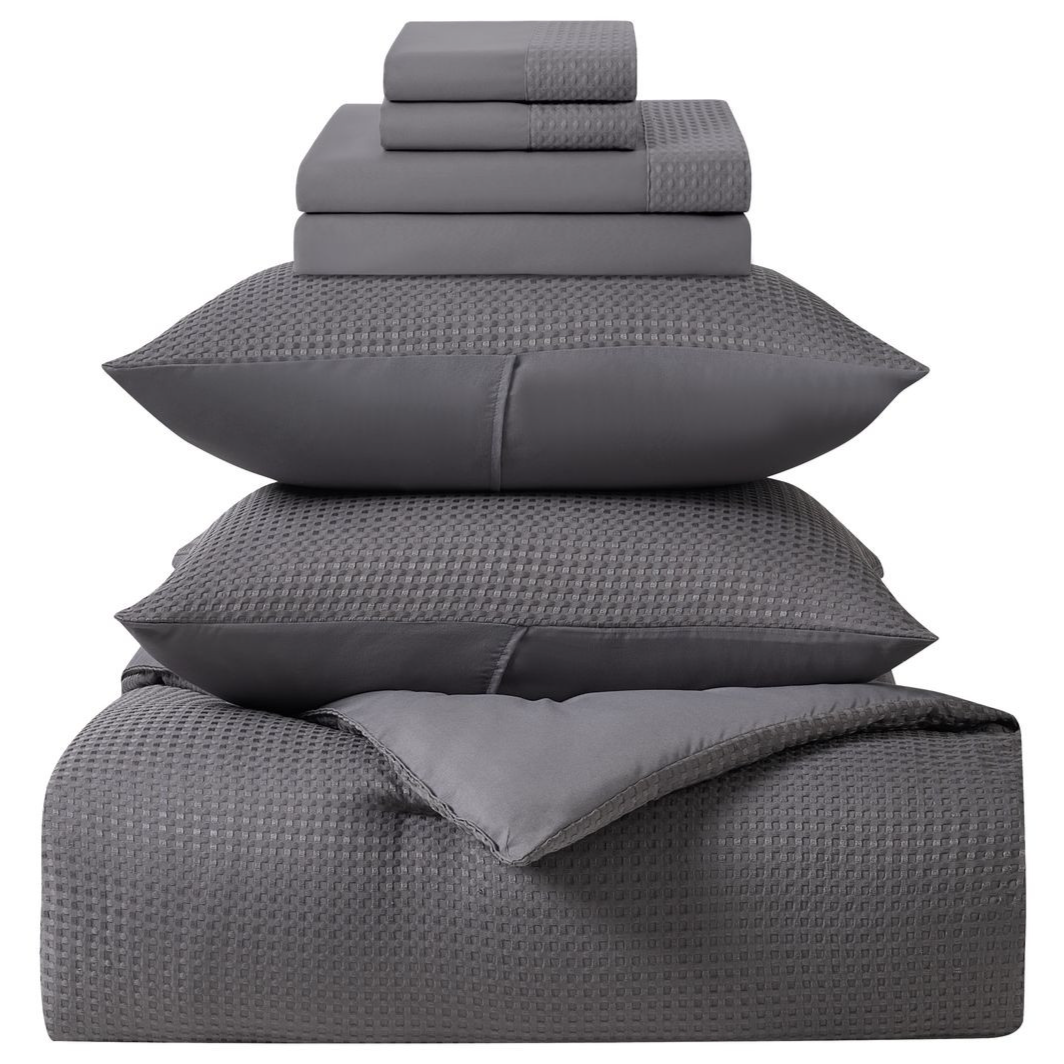 A neatly stacked gray bedding set includes folded sheets, pillowcases with a checkered pattern, and a comforter.