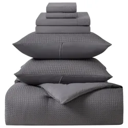 A neatly stacked gray bedding set includes folded sheets, pillowcases with a checkered pattern, and a comforter.
