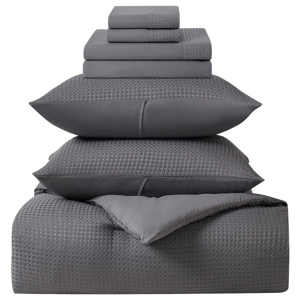 A neatly stacked gray bedding set includes folded sheets, pillowcases with a checkered pattern, and a comforter.