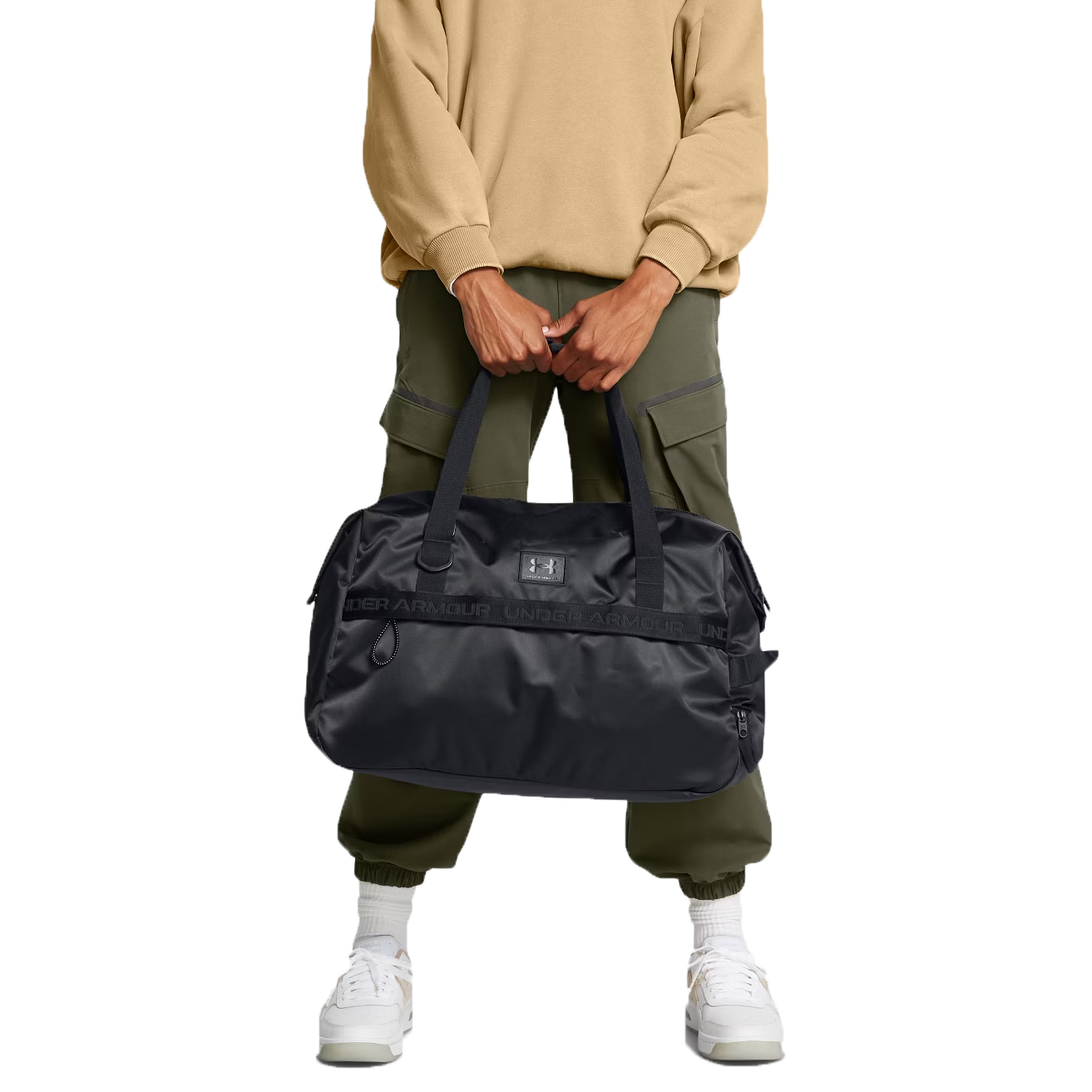 Under Armour Studio Duffel, black, features multiple handles, a spacious interior, and the Under Armour logo. It's paired with olive cargo pants and white sneakers.