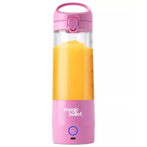 A pink Magic Bullet portable blender filled with orange liquid, featuring a handle, secure top, and power button.