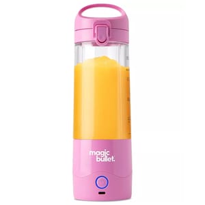 A pink Magic Bullet portable blender filled with orange liquid, featuring a handle, secure top, and power button.