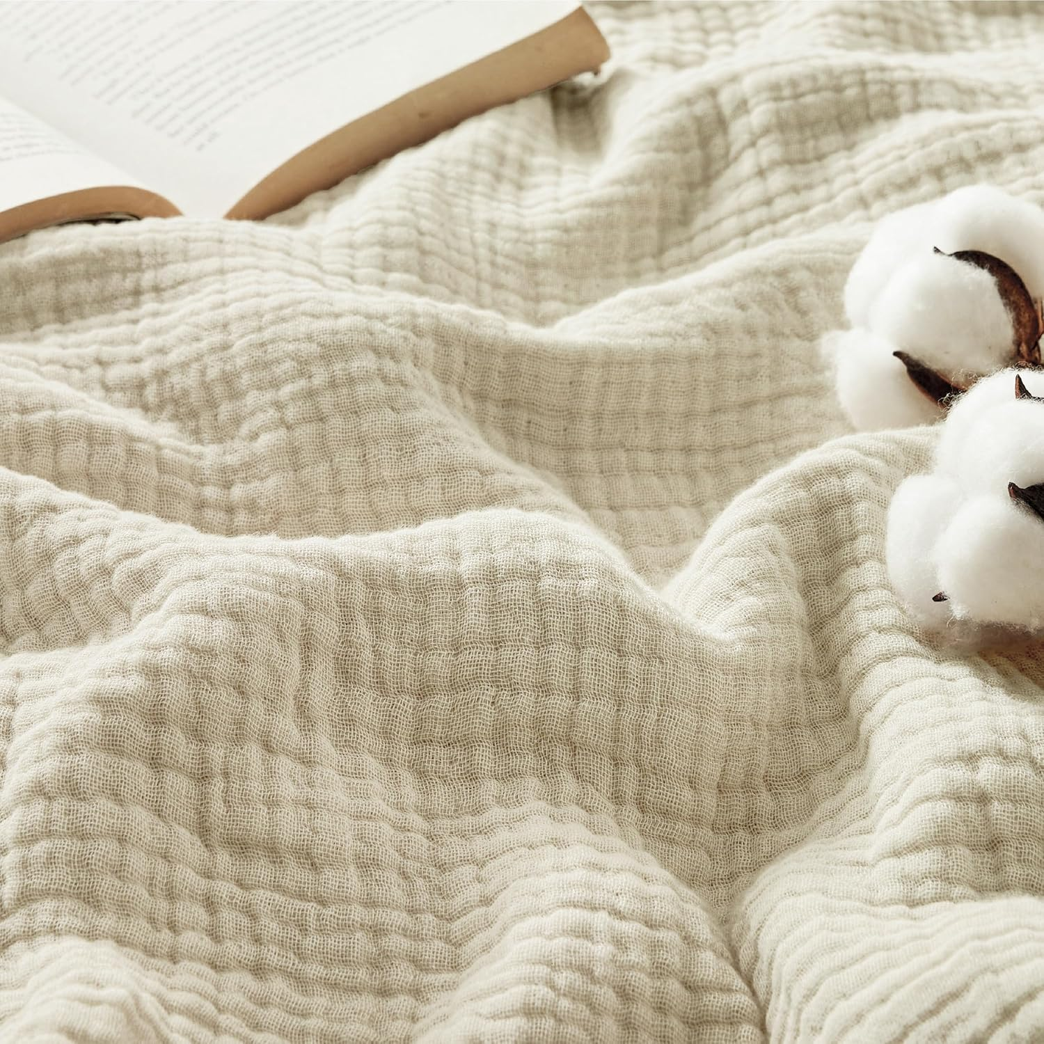 A soft, textured blanket lies next to an open book and cotton branches, highlighting a cozy and natural aesthetic.