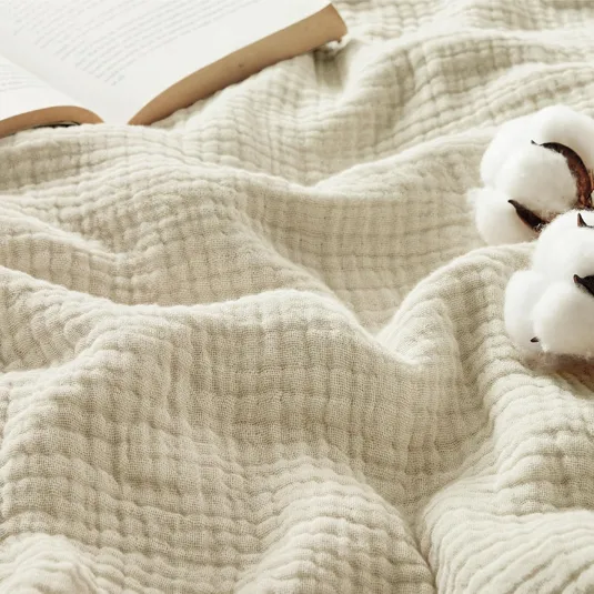 A soft, textured blanket lies next to an open book and cotton branches, highlighting a cozy and natural aesthetic.