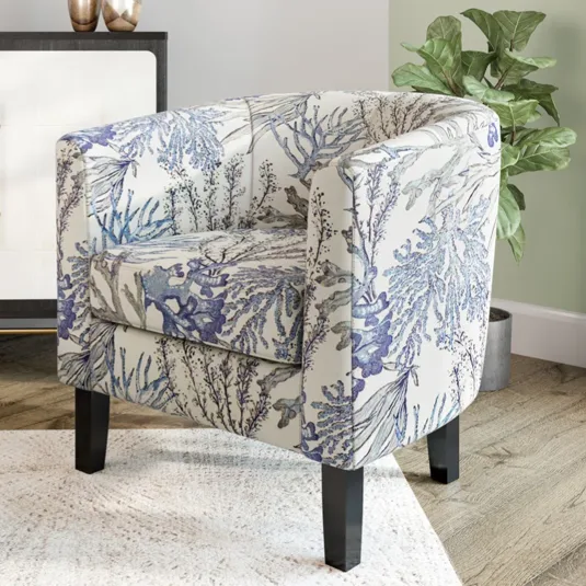 A chair with a floral pattern sits beside a black and white cabinet with brass handles. A marble-topped coffee table and a green plant complete the space.