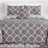 A gray and white comforter set featuring a geometric lattice pattern, including a comforter, two pillow shams, and a decorative pillow.