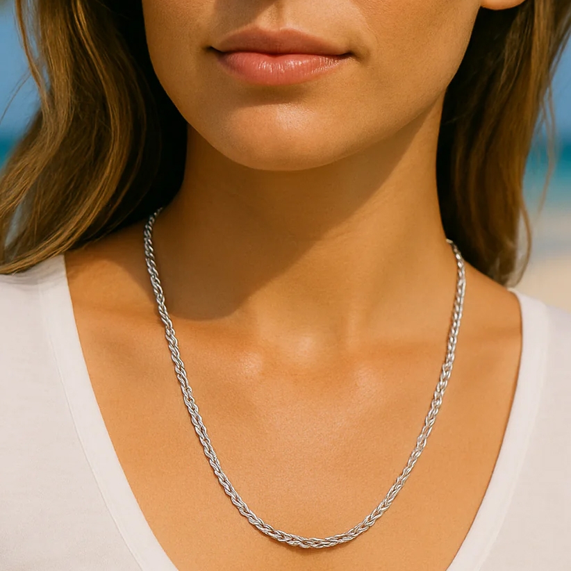 A woman wears a twisted rope-style silver necklace. She is dressed in a white shirt, showcasing the simple and elegant jewelry piece.
