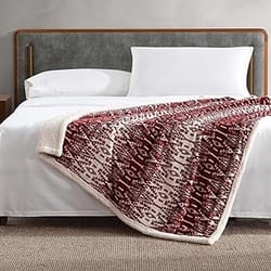 A neatly made bed featuring a dark headboard and white bedding, topped with a red and white patterned throw blanket, displayed in a modern bedroom setting with a carpeted floor.