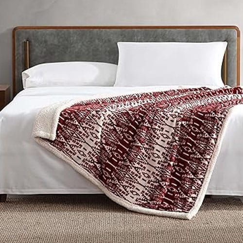 A neatly made bed featuring a dark headboard and white bedding, topped with a red and white patterned throw blanket, displayed in a modern bedroom setting with a carpeted floor.