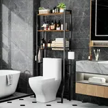 A bathroom features a toilet with a black metal over-the-toilet storage rack holding toiletries, towels, and a plant. Nearby are a bathtub, a marble countertop with a wooden drawer, a mirror, and a toothbrush holder.