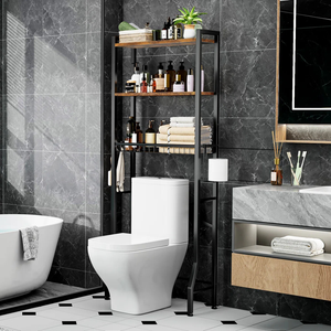 A bathroom features a toilet with a black metal over-the-toilet storage rack holding toiletries, towels, and a plant. Nearby are a bathtub, a marble countertop with a wooden drawer, a mirror, and a toothbrush holder.