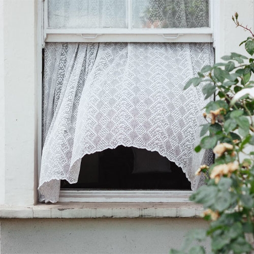 a white wall with a white window and a white curtain blowing in the wind behind a green plant