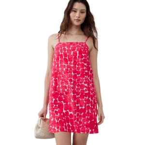 A woman is wearing a red and white sleeveless dress with a spaghetti strap design and a loose, straight cut. She holds a straw handbag, suggesting a casual summer or spring outfit.