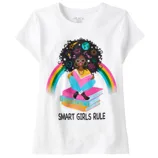 White t-shirt featuring an illustration of a girl sitting on stacked books with rainbow accents. Text reads \“SMART GIRLS RULE\“.