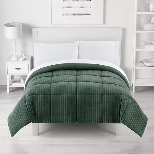 A green, pinstriped comforter is neatly arranged on a white bed frame with white bedding. The room features a white nightstand with a lamp and monochrome decor.
