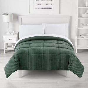 A green, pinstriped comforter is neatly arranged on a white bed frame with white bedding. The room features a white nightstand with a lamp and monochrome decor.