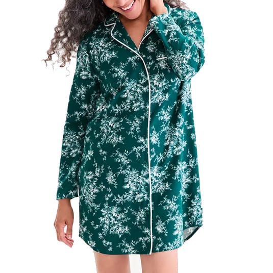 A woman is wearing a green floral-patterned, long-sleeved pajama shirt with white piping.