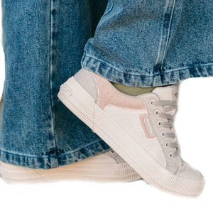 A pair of light-colored sneakers paired with wide-legged blue jeans.