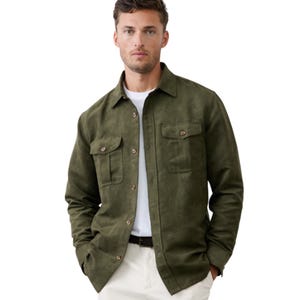 A man is wearing an olive green button-up shirt with front pockets over a white t-shirt and beige trousers.