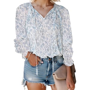 Lightweight boho blouse with a blue floral pattern, featuring long sleeves with ruched cuffs and a V-neck with tassel ties, paired with distressed denim shorts.