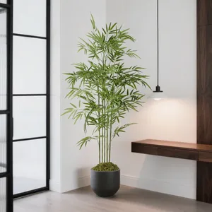 Tall artificial bamboo plant in a black pot, placed in a modern interior with a pendant light and wooden wall accent.