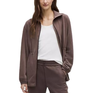 A woman is wearing a brown velour tracksuit with a zip-up jacket and matching pants, paired with a white t-shirt underneath.