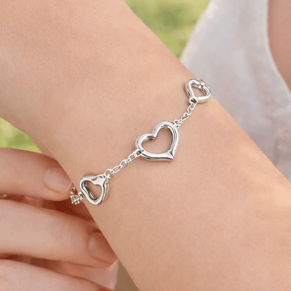 A silver bracelet features three linked heart-shaped charms connected by a delicate chain.