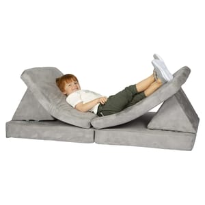 A child is lying on a light gray foam couch for kids with versatile foldable cushions that can be arranged in various shapes for seating or lounging.