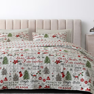 A holiday-themed quilt with matching pillow shams featuring festive phrases and designs, such as Christmas trees, poinsettias, and ornaments, in red, green, and white.