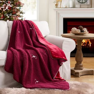A plush red blanket with decorative designs is draped over a white armchair next to a fireplace, set in a cozy living room with Christmas decor.