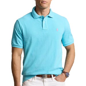 A man wears a light blue polo shirt paired with white pants, a brown belt, and a watch.